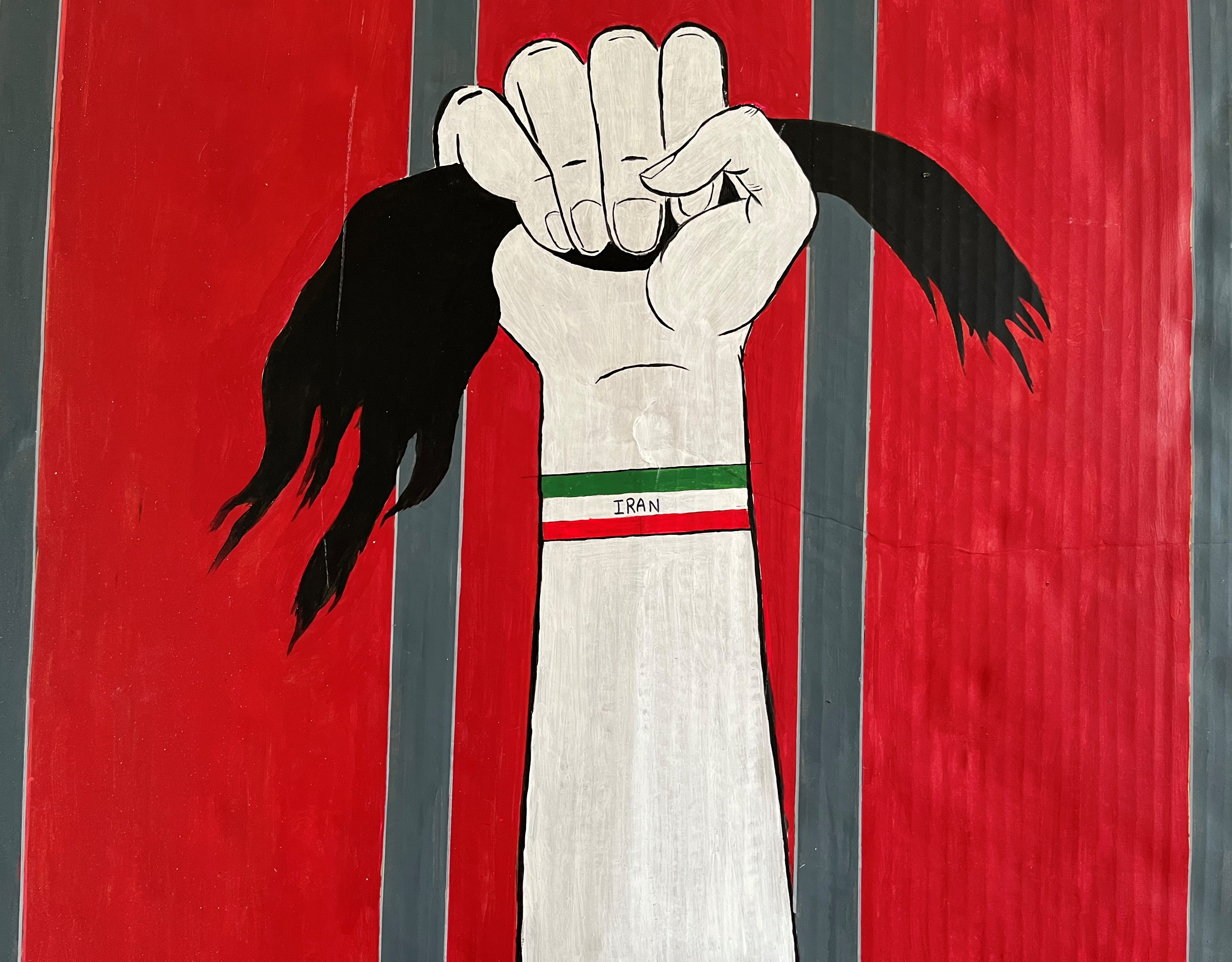 Bersama artwork Iran, a fist holds a clump of hair and a bracelet with the word IRAN is seen on the wrist, the background is bright red